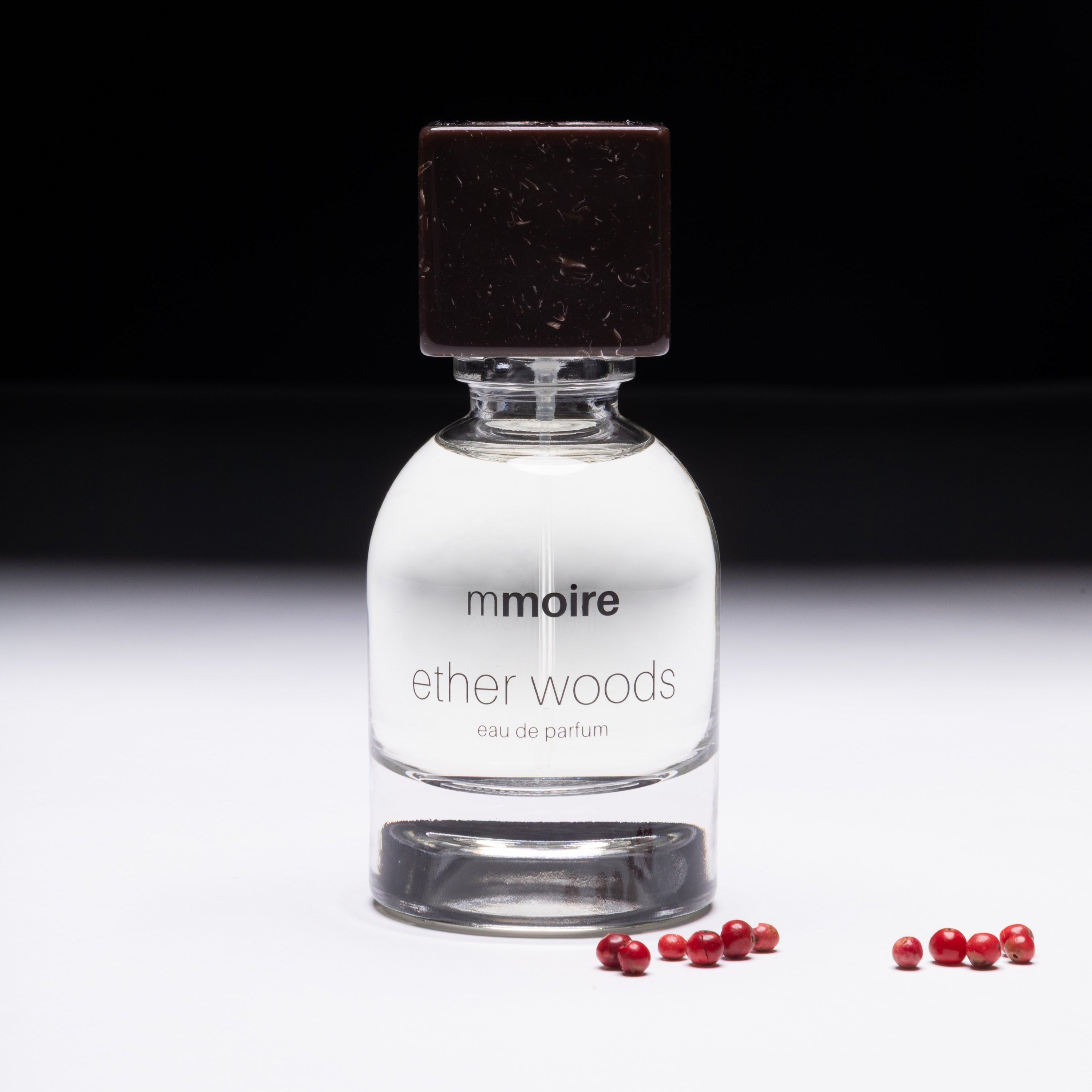 Perfume bottle labeled 'ether woods' by 'mmoire' on a dark background