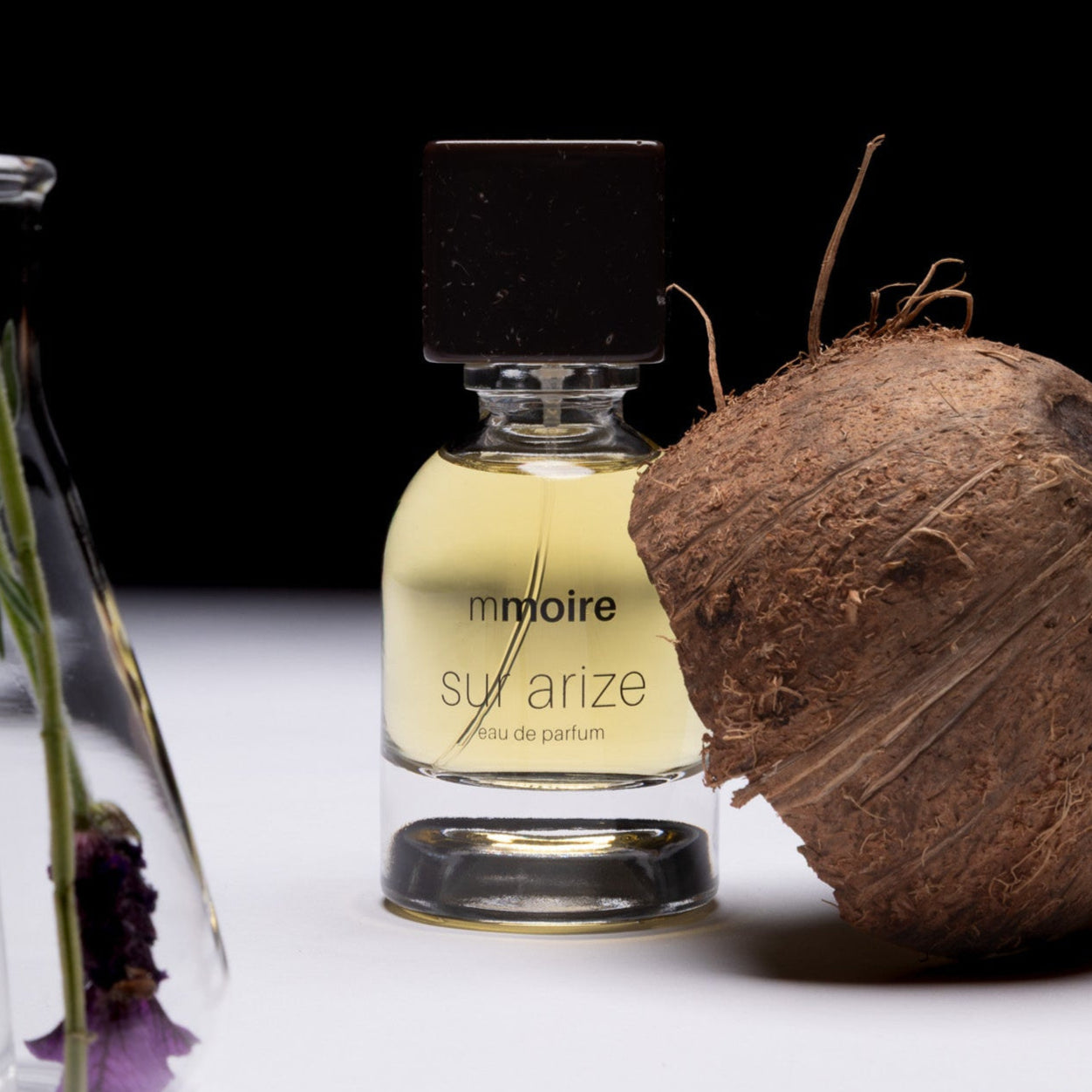 Perfume bottle labeled 'mmoire sur arize' next to a coconut on a white surface with a black background